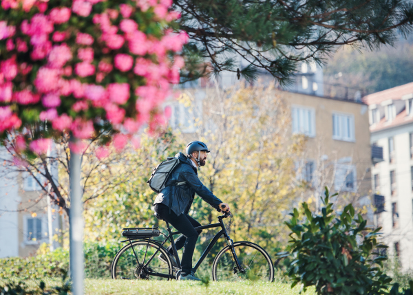 A side view of hipster businessman commuter with bicycle traveling to work in city.