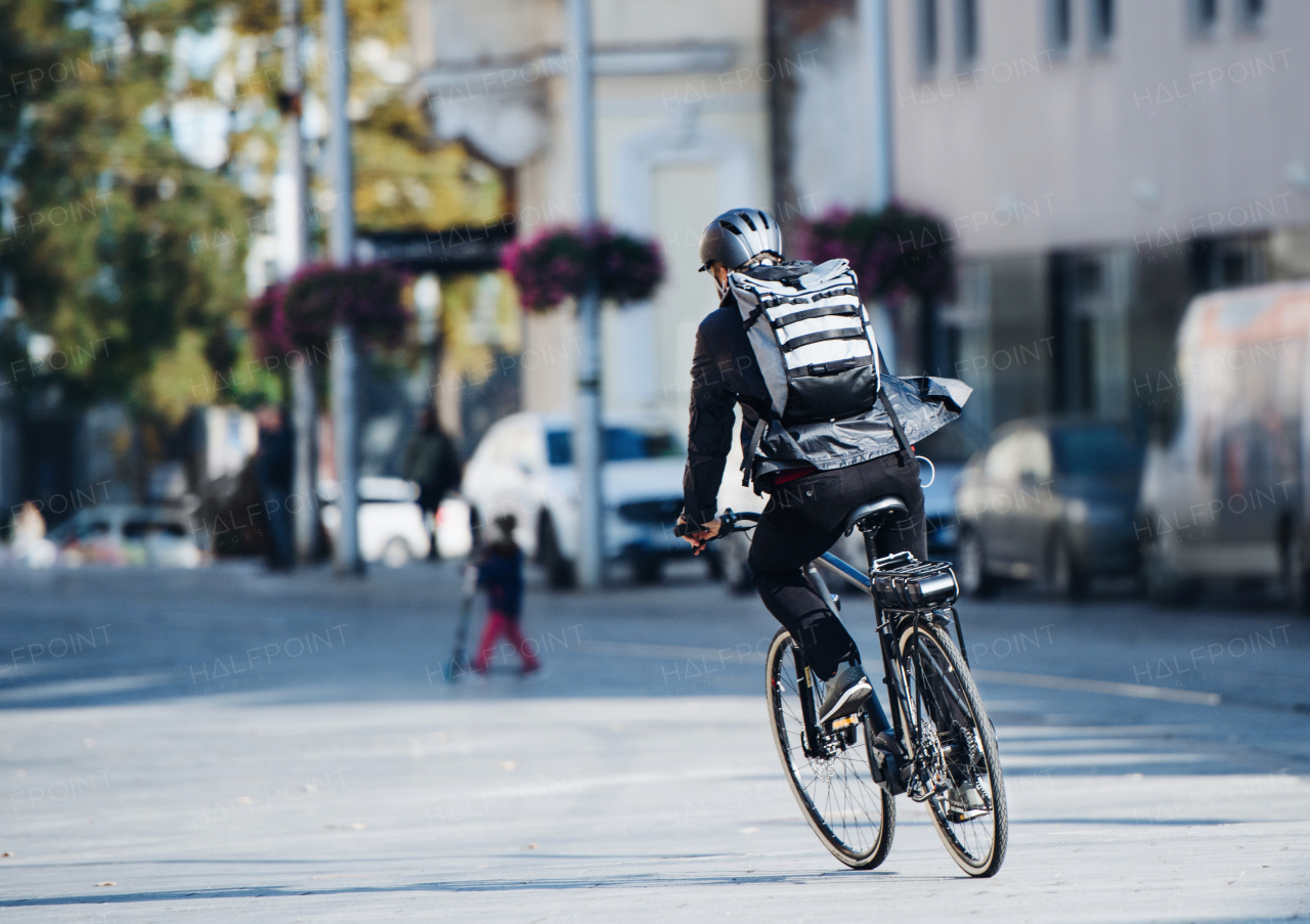 A rear view of male bicycle courier cycling in city, delivering packages. Copy space.