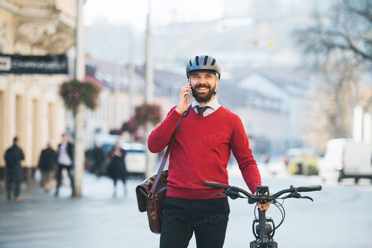 Hipster businessman commuter with bicycle on the way to work in city, standing and using smartphone.