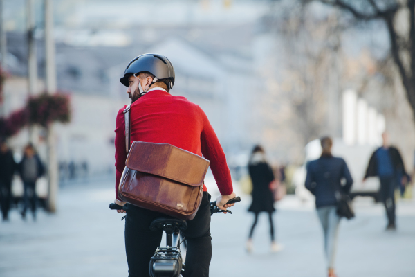 A rear view of a businessman commuter with electric bicycle traveling to work in city. Copy space.