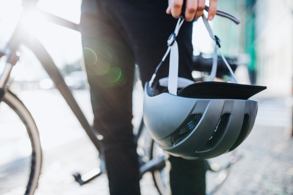 Midsection of man commuter or courier with electric bicycle in city, holding helmet.