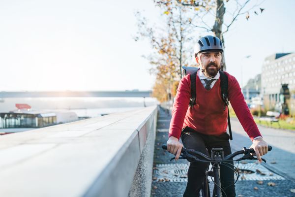 A front view of hipster businessman commuter with electric bicycle traveling to work in city. Copy space.