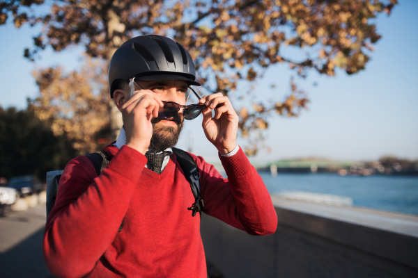 Hipster businessman commuter with bicycle helmet on the way to work in city, putting on sunlglasses.