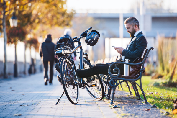 A businessman commuter with bicycle sitting on bench in city and using smartphone when traveling home from work.