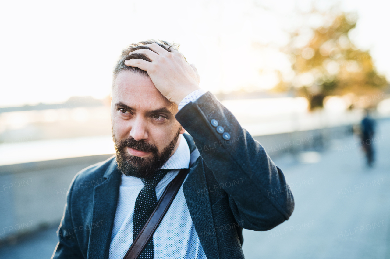 Worried hipster businessman walking in city at sunset. Copy space.