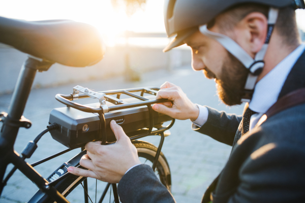 Hipster businessman commuter setting up electric bicycle when traveling home from work in city.