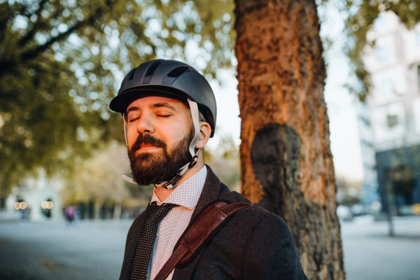 Businessman commuter with helmet standing in city at sunset, eyes closed. Copy space.