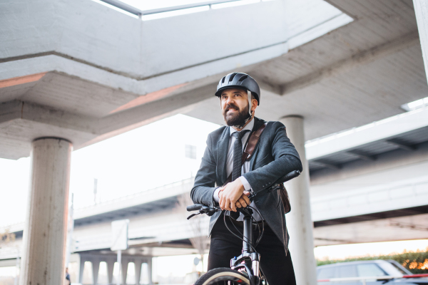 Hipster businessman commuter with electric bicycle traveling home from work in city at sunset. Copy space.