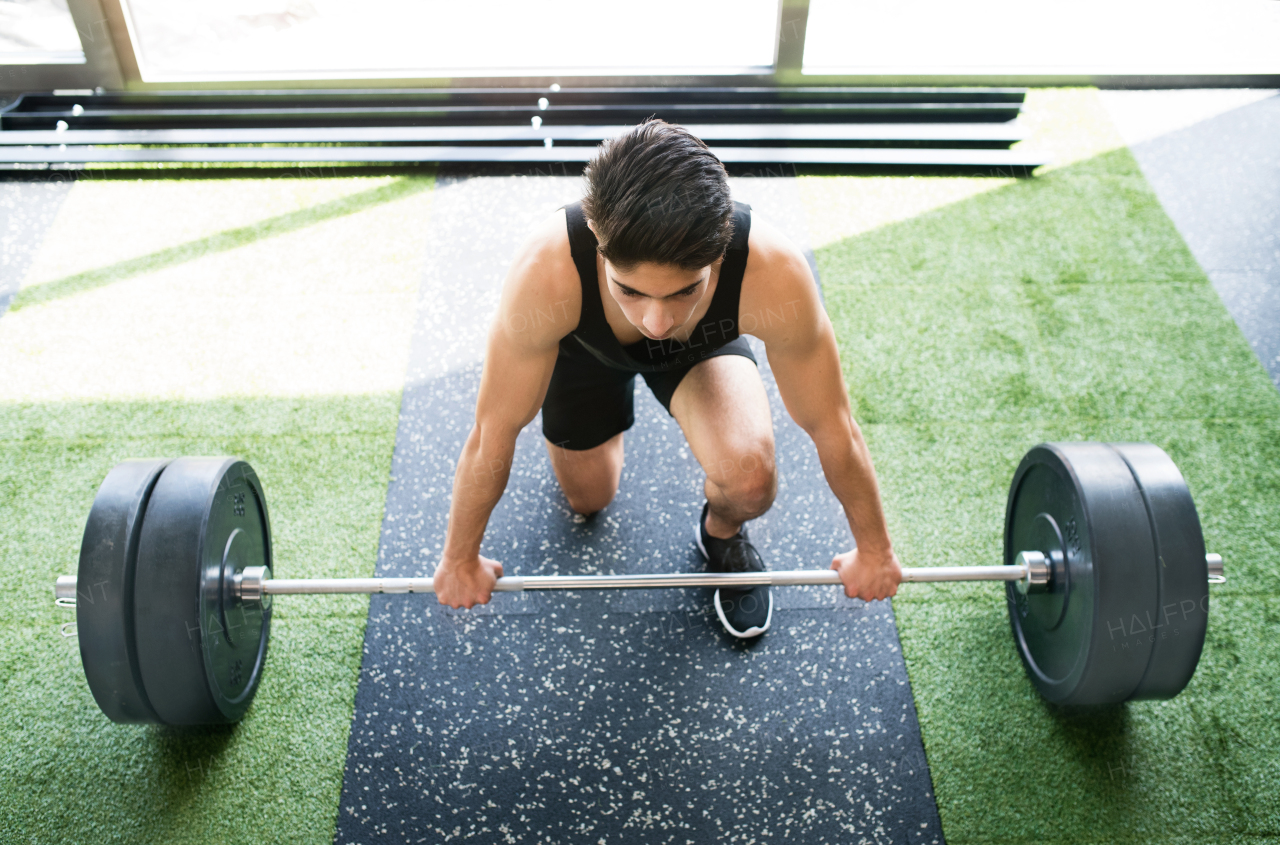 Young fit hispanic man in gym lifting heavy barbell, flexing muscles