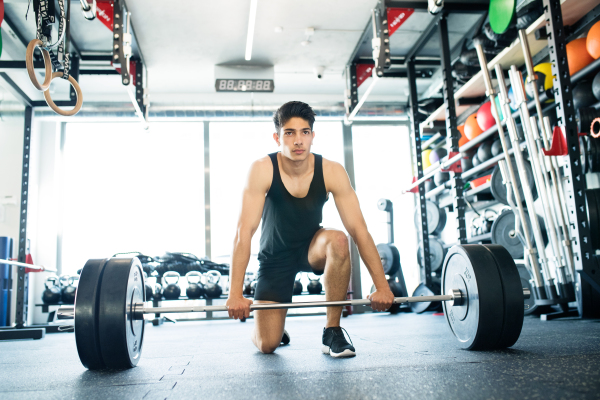 Young fit hispanic man in gym lifting heavy barbell, flexing muscles