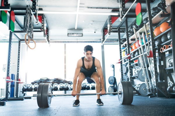 Young fit hispanic man in gym lifting heavy barbell, flexing muscles