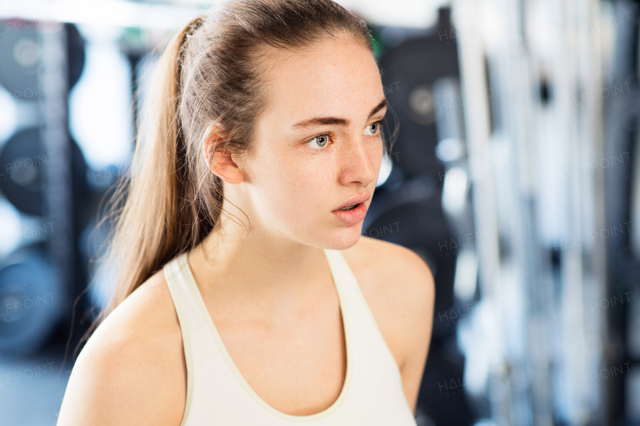 Face of beautiful young fit woman in gym in white tank top, resting