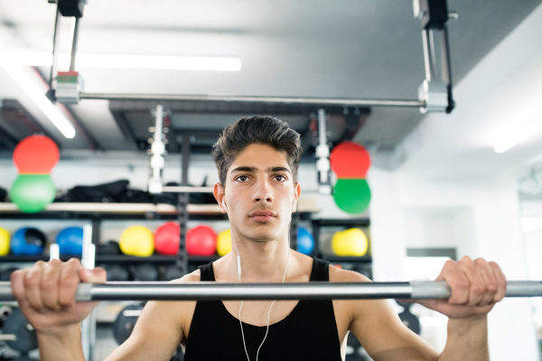 Hispanic fitness man in gym at the heavy barbell, resting, earphones in his ears, listening music