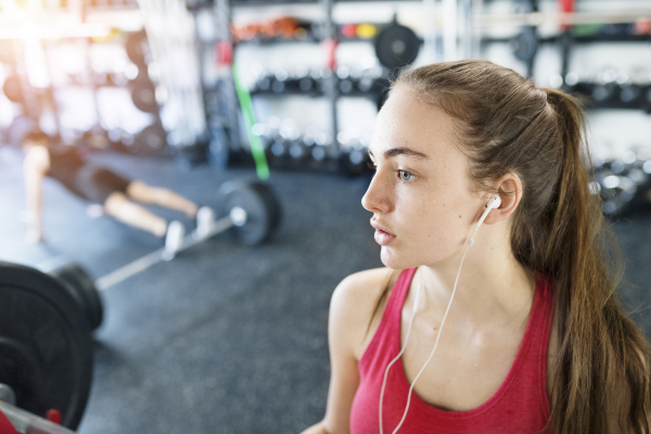 Beautiful young fit woman in gym resting, earphones in her ears, listening music