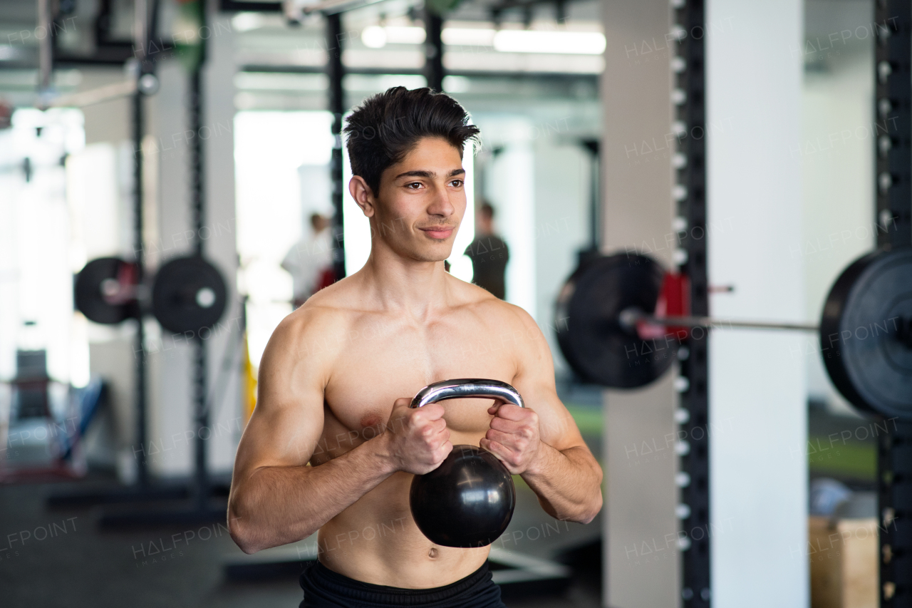 Fit hispanic man doing strength training, exercising with kettlebell in modern gym.