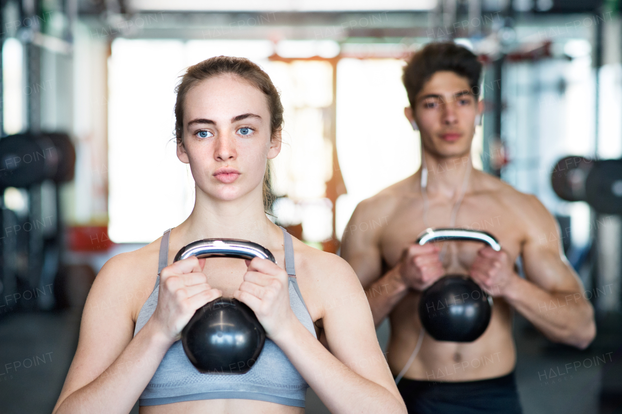 Beautiful young fit couple doing strength training, exercising with kettlebell in modern gym.