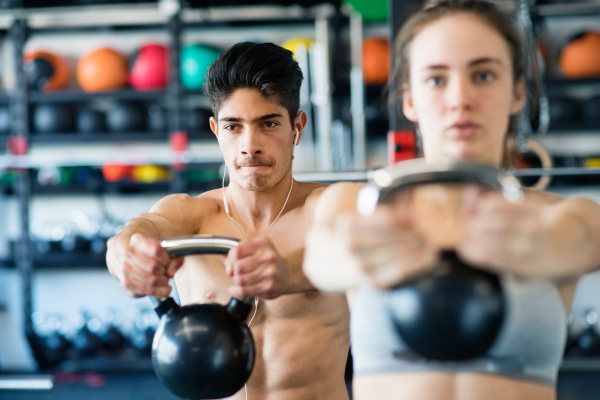 Beautiful young fit couple doing strength training, exercising with kettlebell in modern gym.