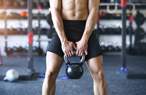 Unrecognizable young fit man in modern gym doing kettlebell swings. Close up.