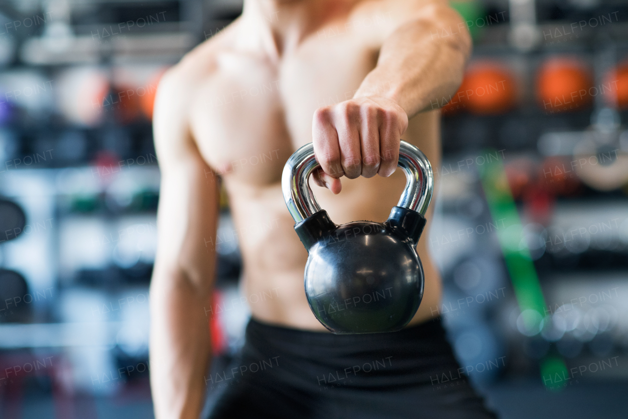 Unrecognizable young fit man in modern gym doing kettlebell swings. Close up.