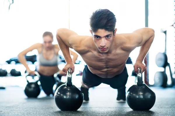 Beautiful young fit couple doing strength training, doing push ups on kettlebells in modern gym