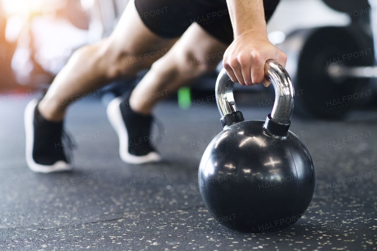 Unrecognizable young fit man doing strength training, doing push ups on kettlebells in modern gym.