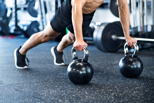 Unrecognizable young fit man doing strength training, doing push ups on kettlebells in modern gym.