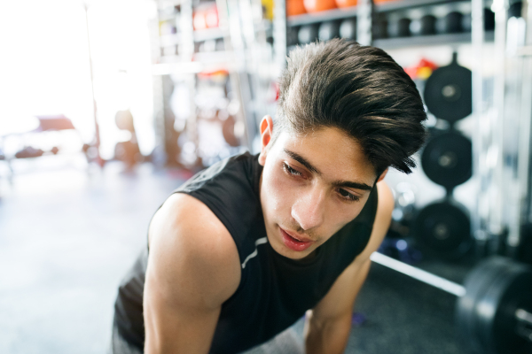 Young fit hispanic man in black sleeveless shirt in modern crossfit gym resting