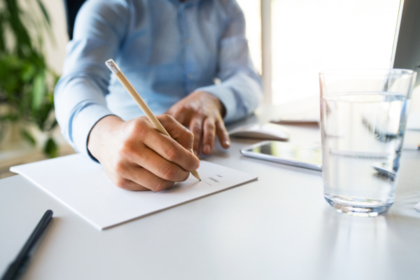 Unrecognizable young businessman in his office, sitting at the desk, writing.