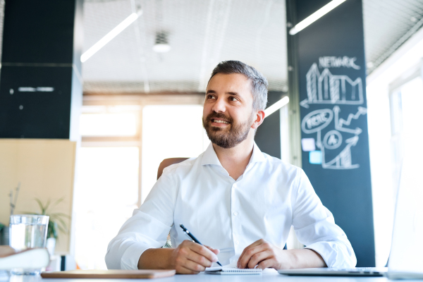 Handsome young businessman in his office, sitting at the desk.