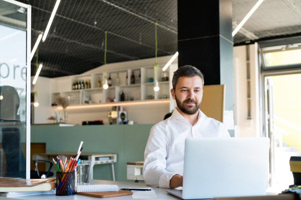 Handsome young businessman working in his office, sitting at the desk, laptop and tablet in front of him.