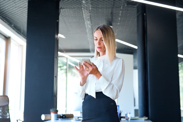 Unrecognizable businesswoman in her office holding smart phone, texting.