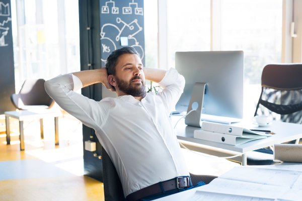 Handsome young businessman in his office, sitting at the desk, having a break.