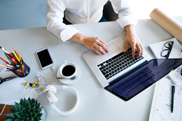 Unrecognizable young businesswoman in her office, sitting at the desk, working on laptop.