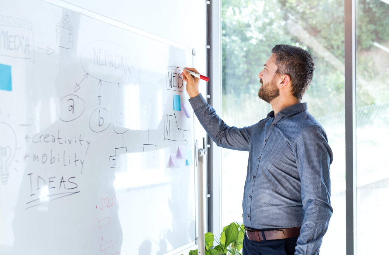 Handsome young businessman with gray hair in the office writing notes on whiteboard, setting goals.