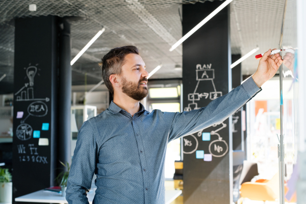 Handsome young businessman with gray hair in the office writing notes on whiteboard, setting goals.