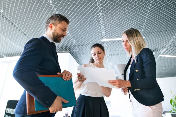 Three business people in the workplace. Two women and man standing in the office talking together.