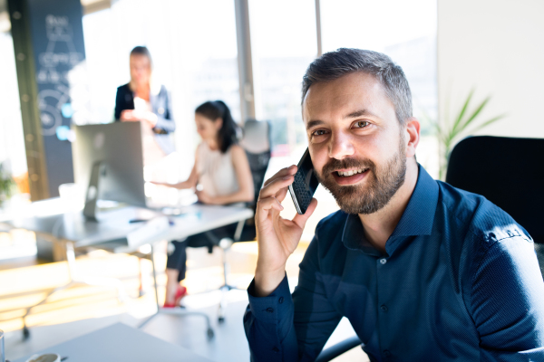 Three business people in the office working together. Businessman with smart phone making a phone call.