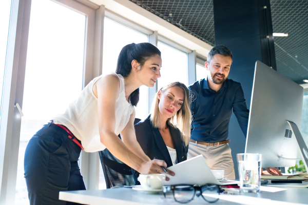 Three attractive young business people in the office working together, consulting a project.