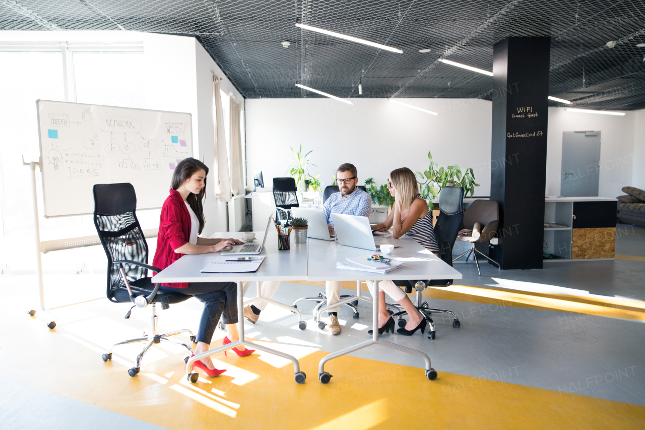 Three business people in the workplace. Two women and man sitting in the office working together.