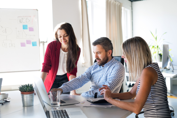 Three business people in the workplace. Two women and man sitting in the office working together, discussing a project.