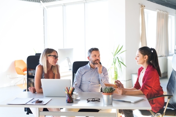 Three business people in the workplace. Two women and man sitting in the office talking together.