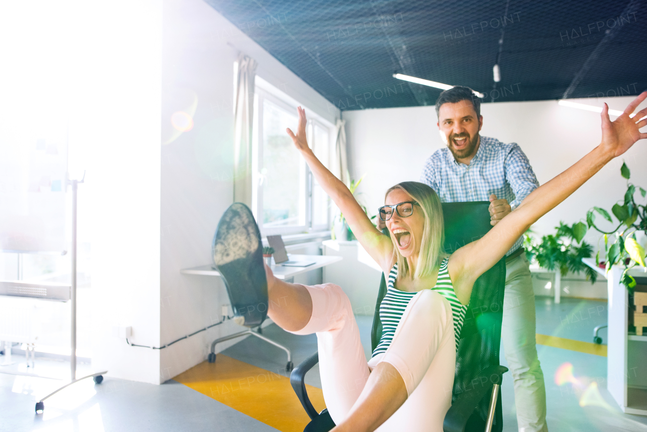 Young attractive business people in the office having fun, man pushing woman sitting on chair.