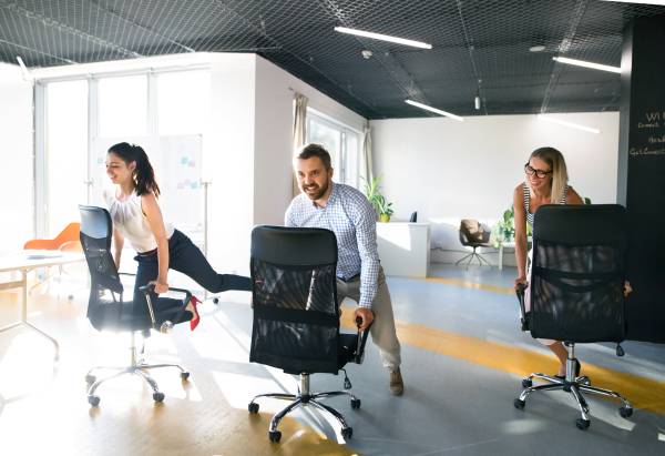 Young attractive business people riding a chair and racing in the workplace.