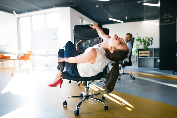 Young attractive business woman riding a chair and turning around in the workplace.