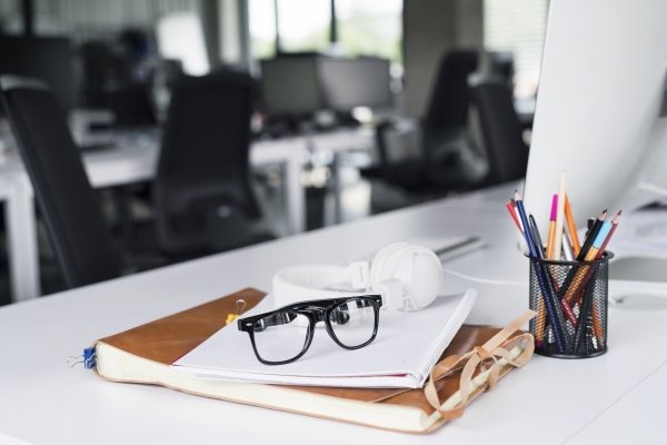 Office desk with computer, notebook, headphones, eyeglasses and pens. The interior of workspace.