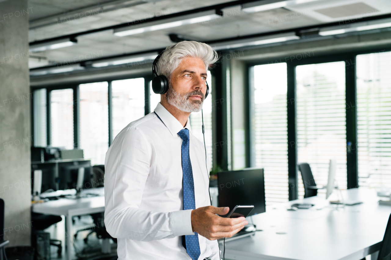 Mature businessman with headphones in the office listening to music.