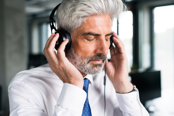 Mature businessman with headphones in the office listening to music.