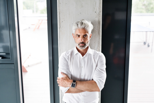 Handsome mature businessman with gray hair in the office wearing white shirt, arms crossed.