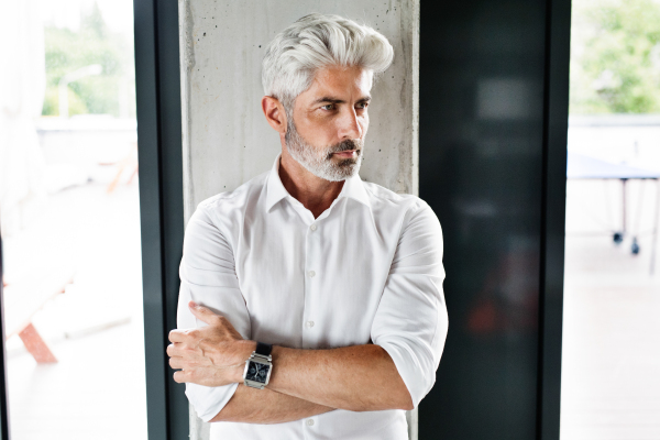 Handsome mature businessman with gray hair in the office wearing white shirt, arms crossed.