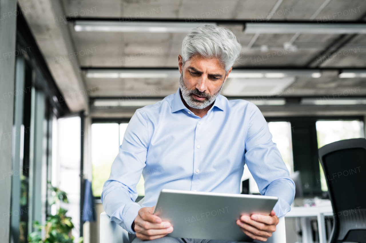 Mature businessman with tablet in the office, reading.